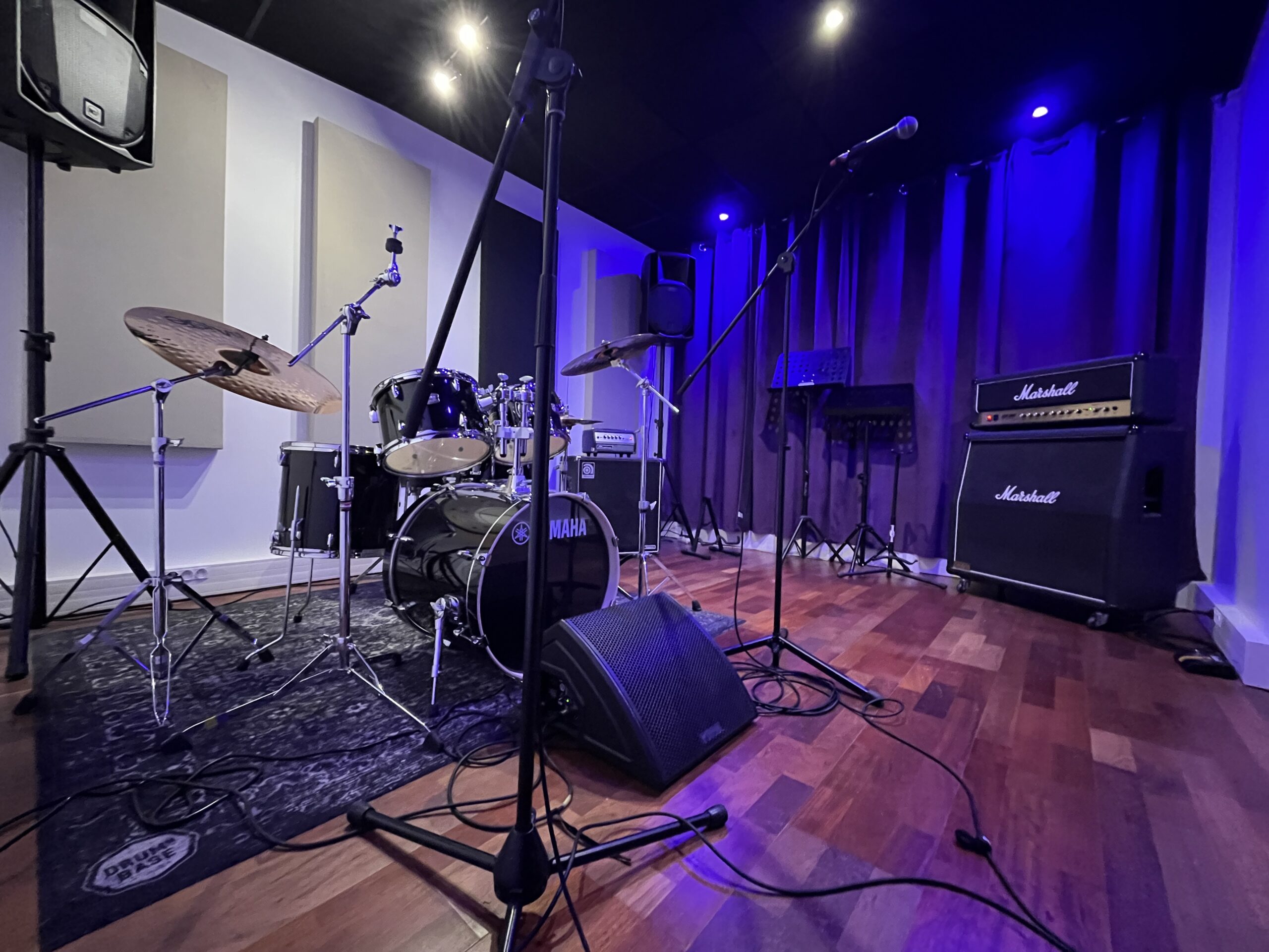 Vue du studio 4 avec batterie, pieds de microphones et amplificateur Marshall sous un éclairage bleu.